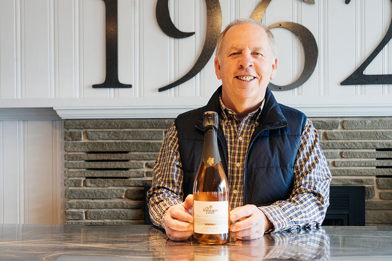 Allyn Brand smiling and holding a bottle of wine.