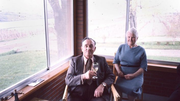 Dr. Frank holding a wine glass with Eugenia on their front porch.