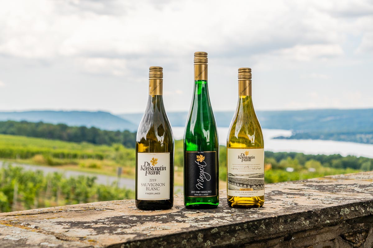 Three bottles of wine with a lake and vineyard in the background.