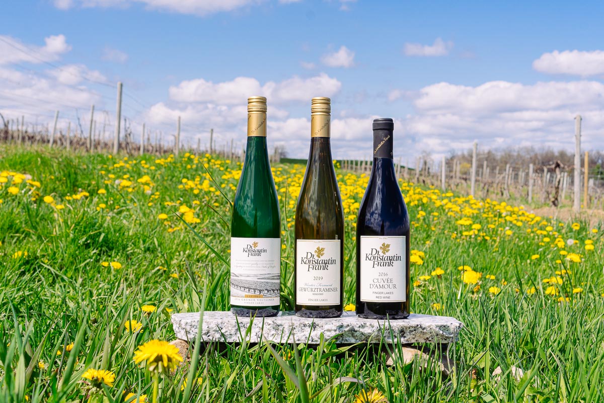 Three wine bottles sitting on a rock with yellow flowers in the background.