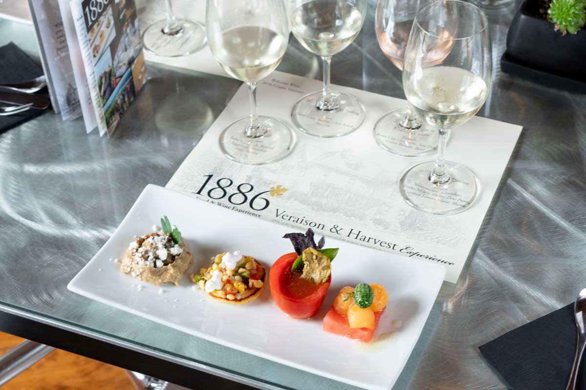 A plate of four small food portions with a placemat with four wine glasses.