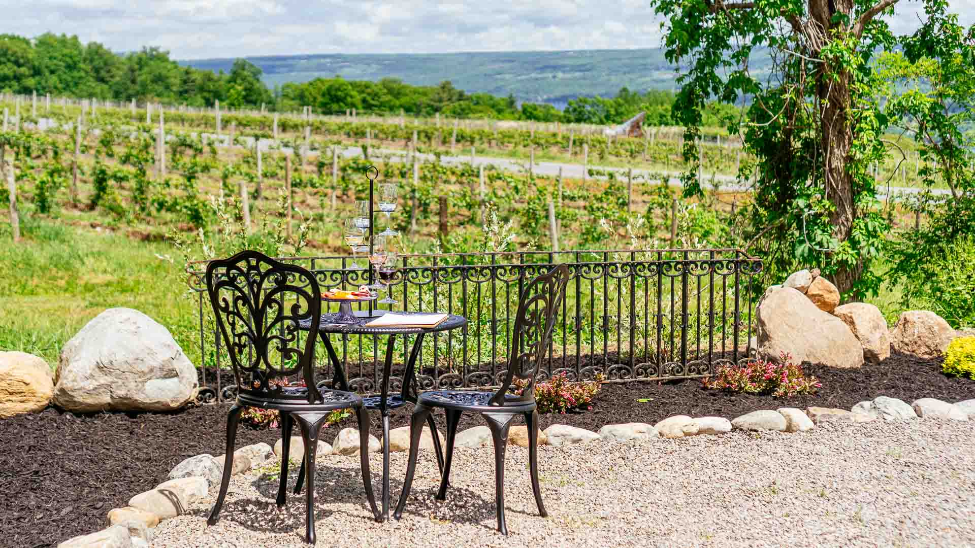 A set of black metal garden furniture with a flight of wine and a cheese board on top.