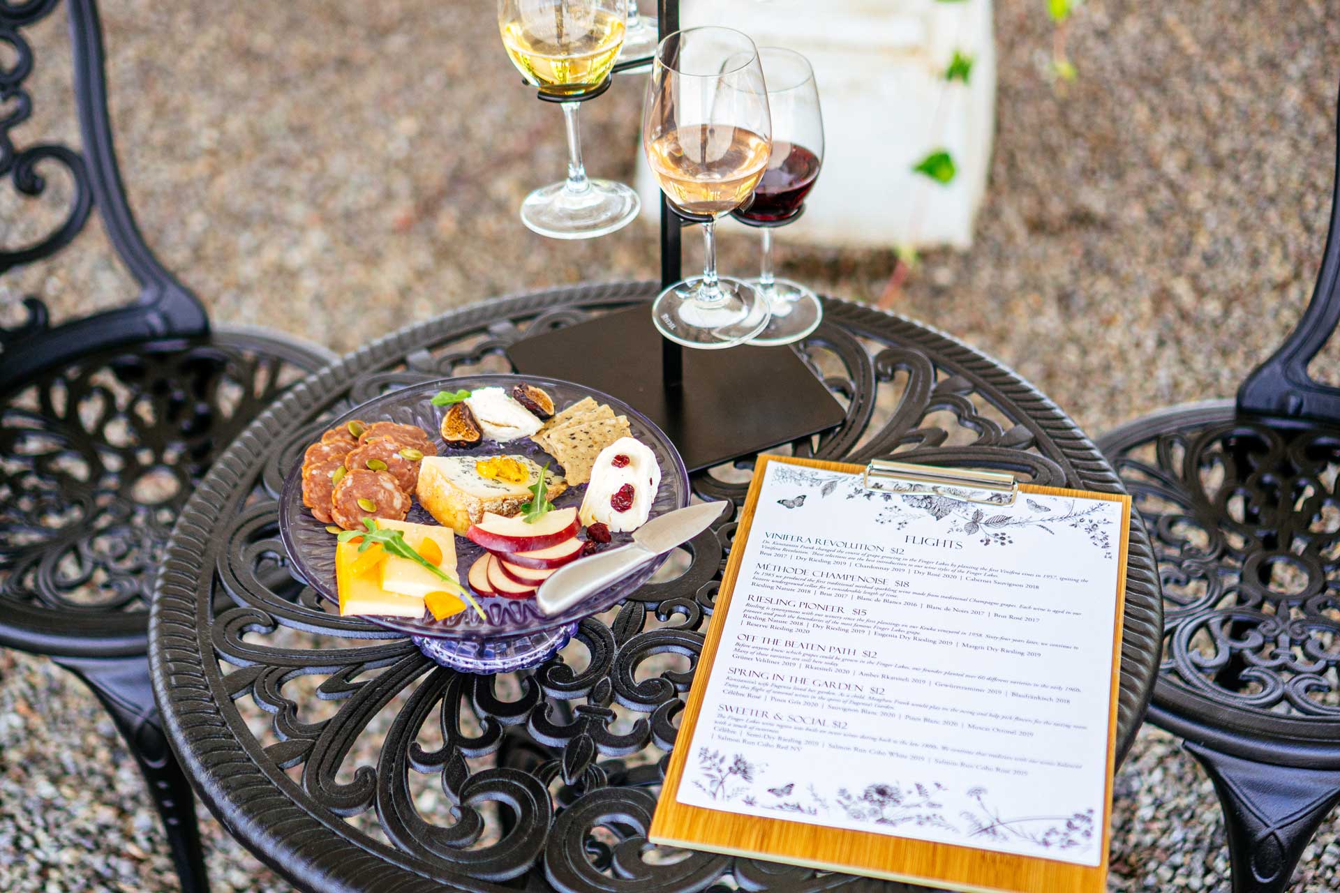 A flight carrier with wine glasses, a charcutier board, and a menu in a clipboard.