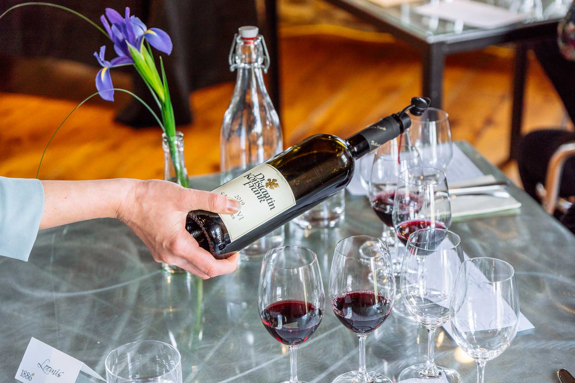 A bottle of red wine being poured into several glasses.