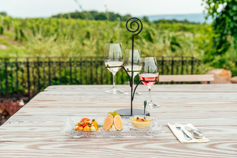 A flight carrier with three wines and a plate with three food displays.