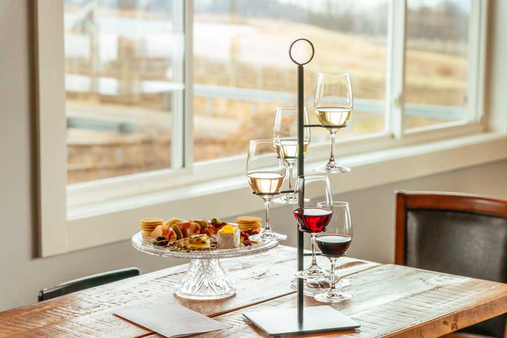 A flight of 5 glasses of wine sitting on a table with a charcuterie board.