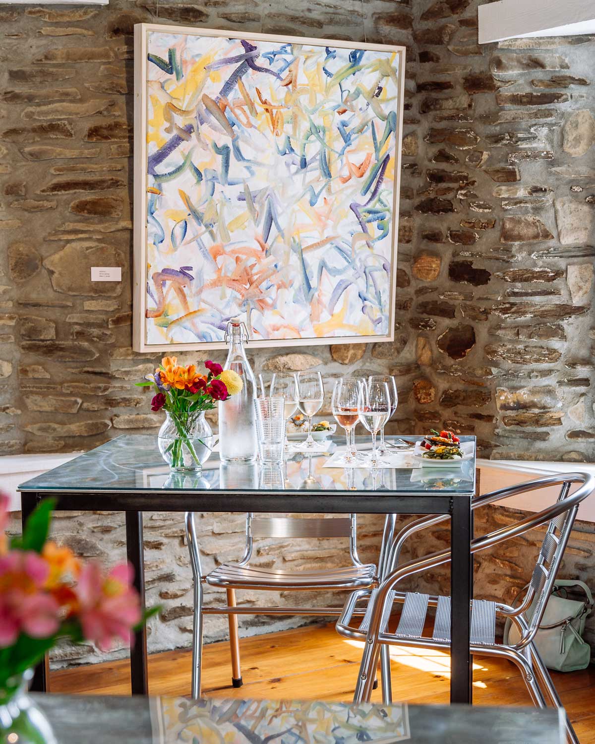 Dinning Table set with wine glasses, food, and flowers with a painting in the background.