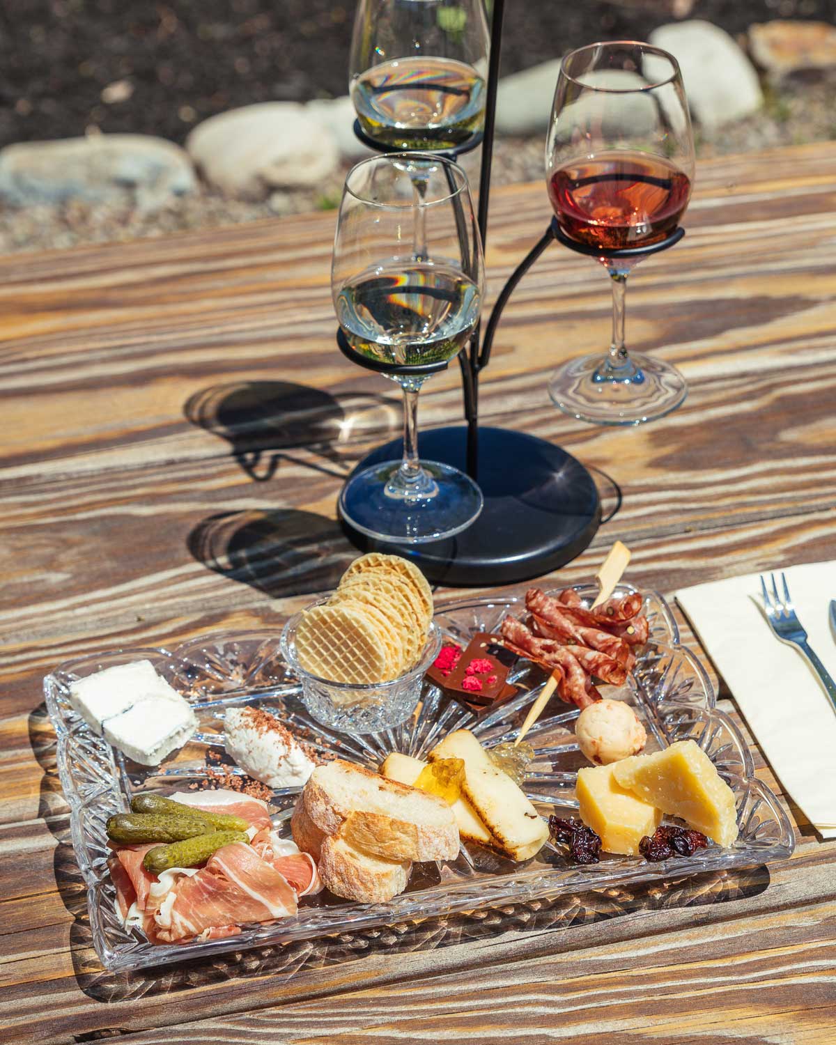 A flight carrier of three glasses of wine and a cheese plate with a variety of charcutier items.