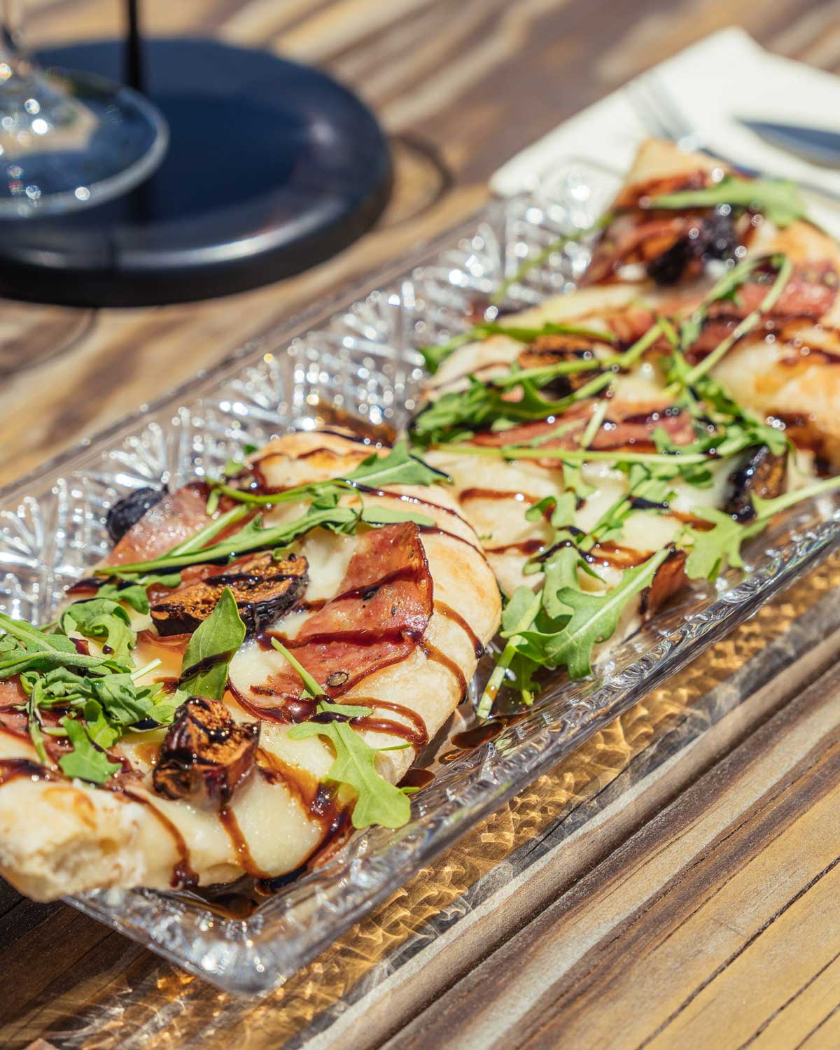 Four slices of flat bread with cheese, arugula, salami, drizzled with balsamic dressing